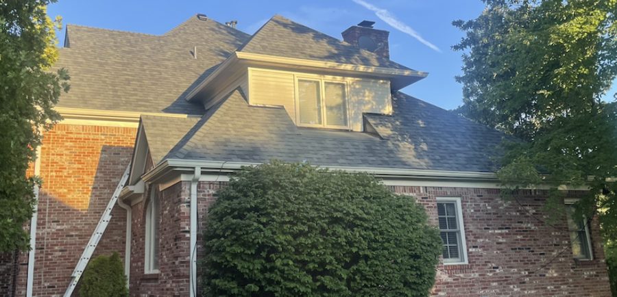 Brick two-story home with a ladder up against a newly shingled roof and chimney