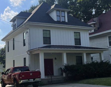 Home with white siding, dark roof, and standing-seam metal porch roof