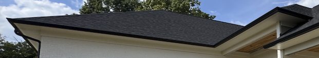 Close-up of a dark architectural shingle roofline with new black gutters against a blue sky